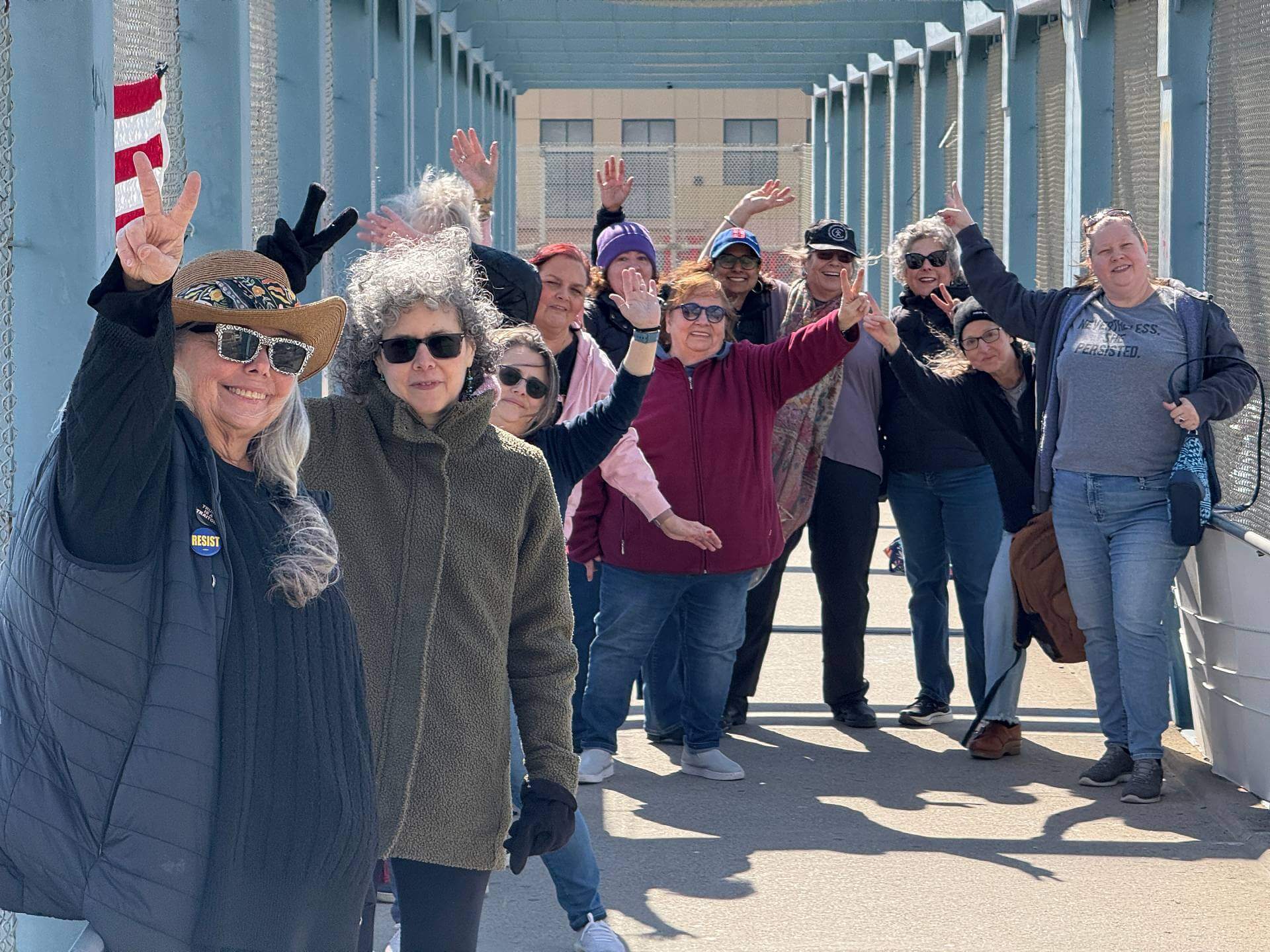 A group of happy protesters standing on a highway overpass smiling and holding up the peace sign on their fingers
